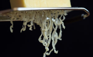 An image of Truly Grass Fed Sharp cheddar being shredded by a grater